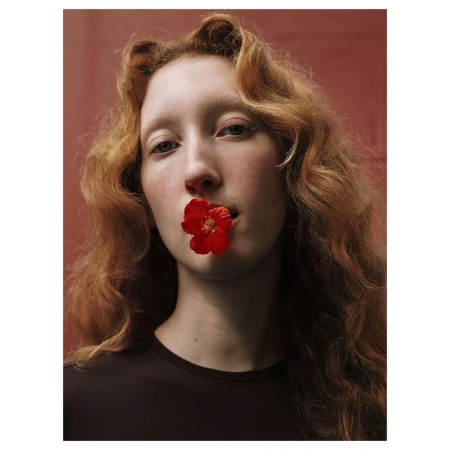 Portrait of a woman with long red hair holding a bright red flower in her mouth by photographer Virginie Khateeb