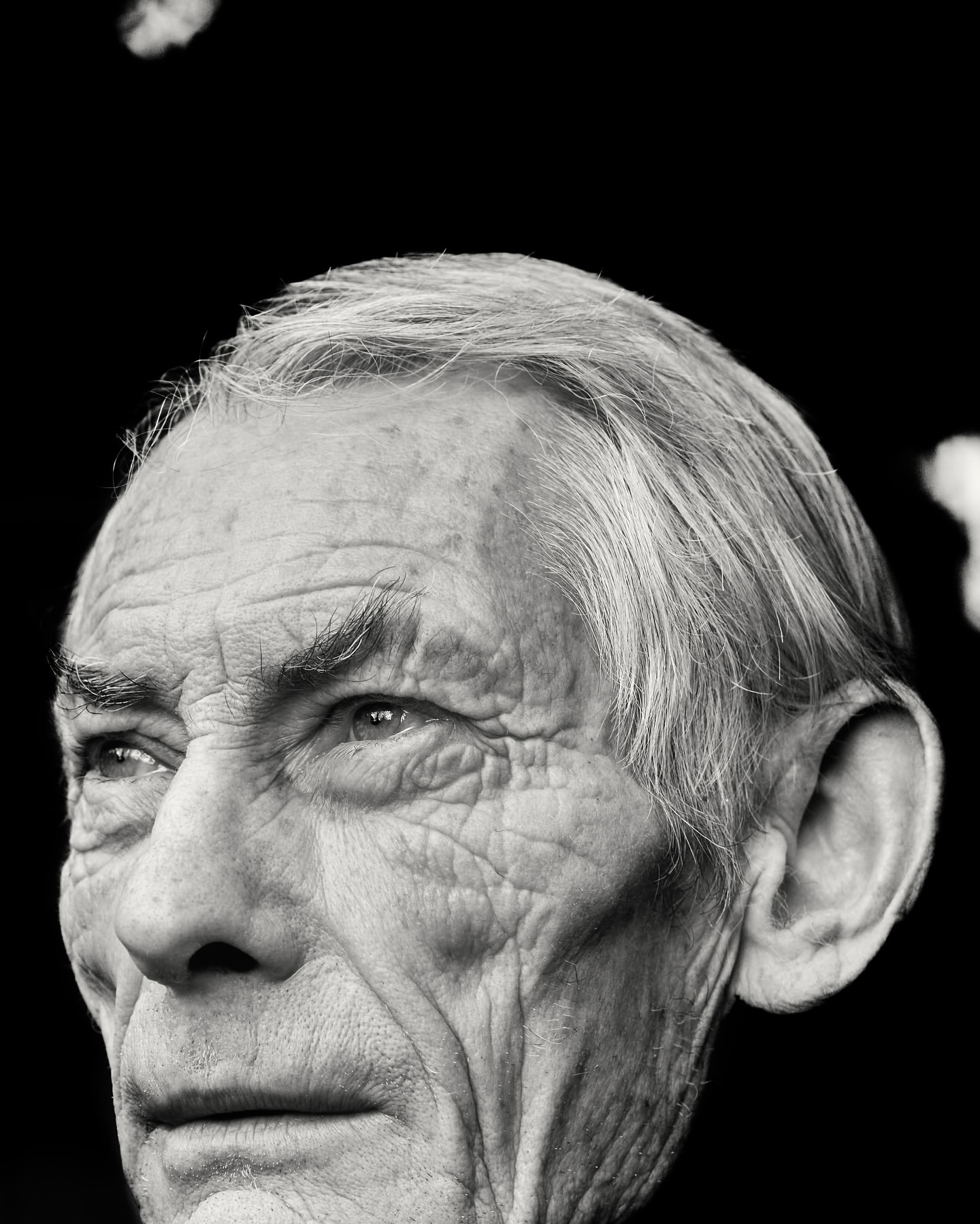 Monochrome portrait of an elderly man with detailed facial features, showcasing a close-up of his face against a dark background.