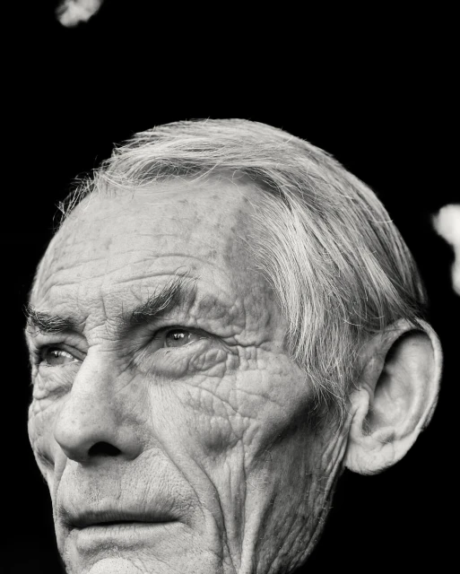 Monochrome portrait of an elderly man with detailed facial features, showcasing a close-up of his face against a dark background.