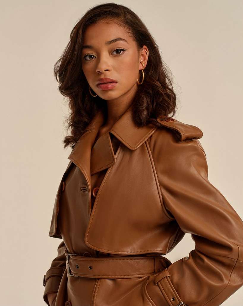 Headshot of an African-American woman with brown hair and gold hoop earrings wearing a brown leather trench coat against a beige backdrop.