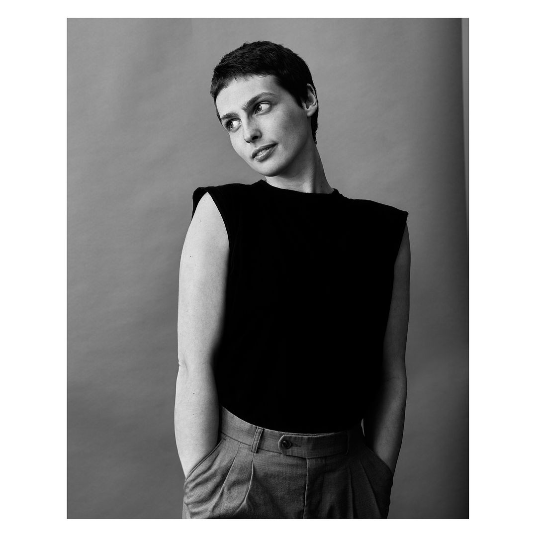 Studio portrait of a confident woman with short dark hair in a black top and grey pants against a grey background. Fashion and style.