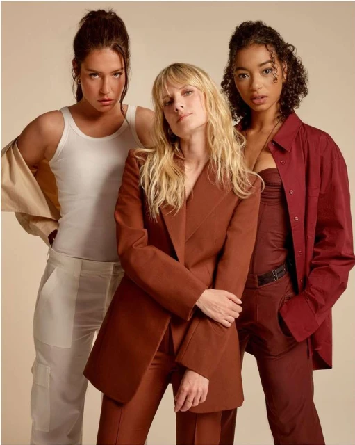Three diverse women in stylish suits pose in a studio shot.  Blonde hair, brown hair, and a confident look with neutral colors dominate.
