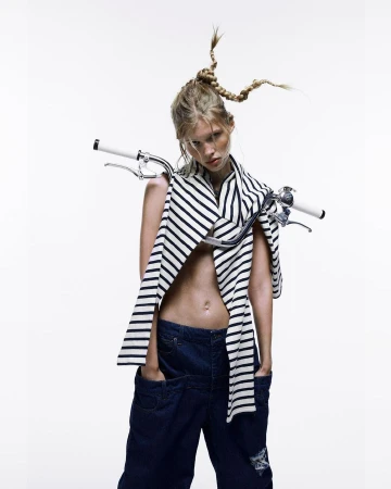 Fashion shot of a woman with a unique braided hairstyle, wearing a striped shirt and denim pants, with bicycle handlebars around her neck.