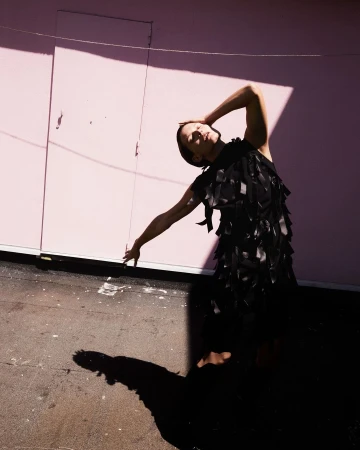Model in a black dress posing against a pink wall with harsh diagonal shadows captured by photographer Vito Fernicola.