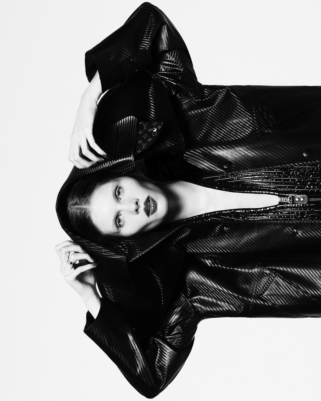 Model wearing a black hooded coat with hands raised against a white background