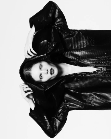 Model wearing a black hooded coat with hands raised against a white background