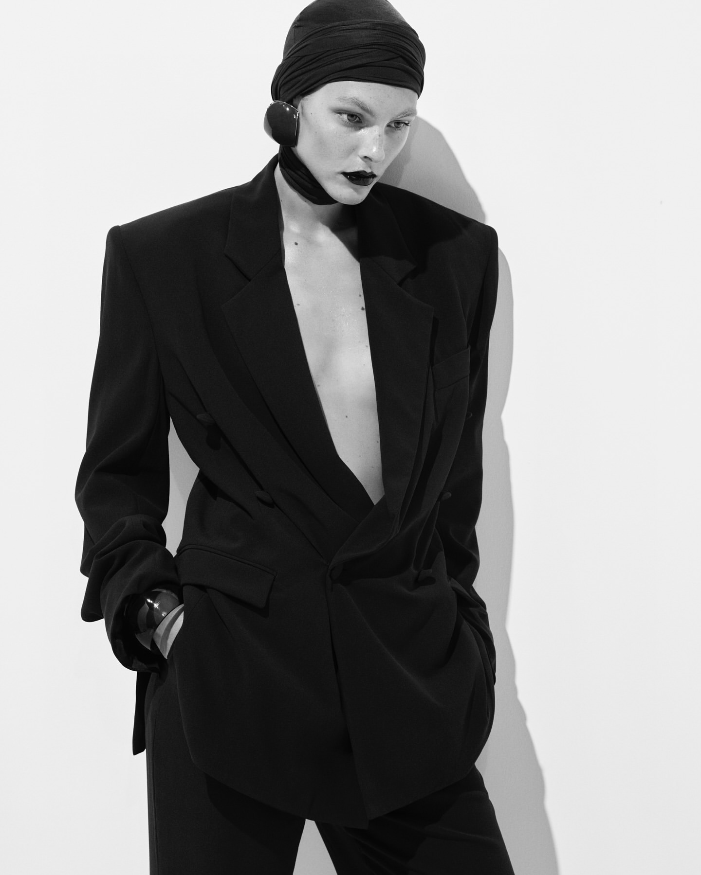 Monochrome fashion portrait of a model in an oversized black blazer and fitted headwrap against a plain white background