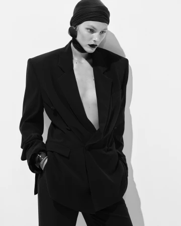 Monochrome fashion portrait of a model in an oversized black blazer and fitted headwrap against a plain white background