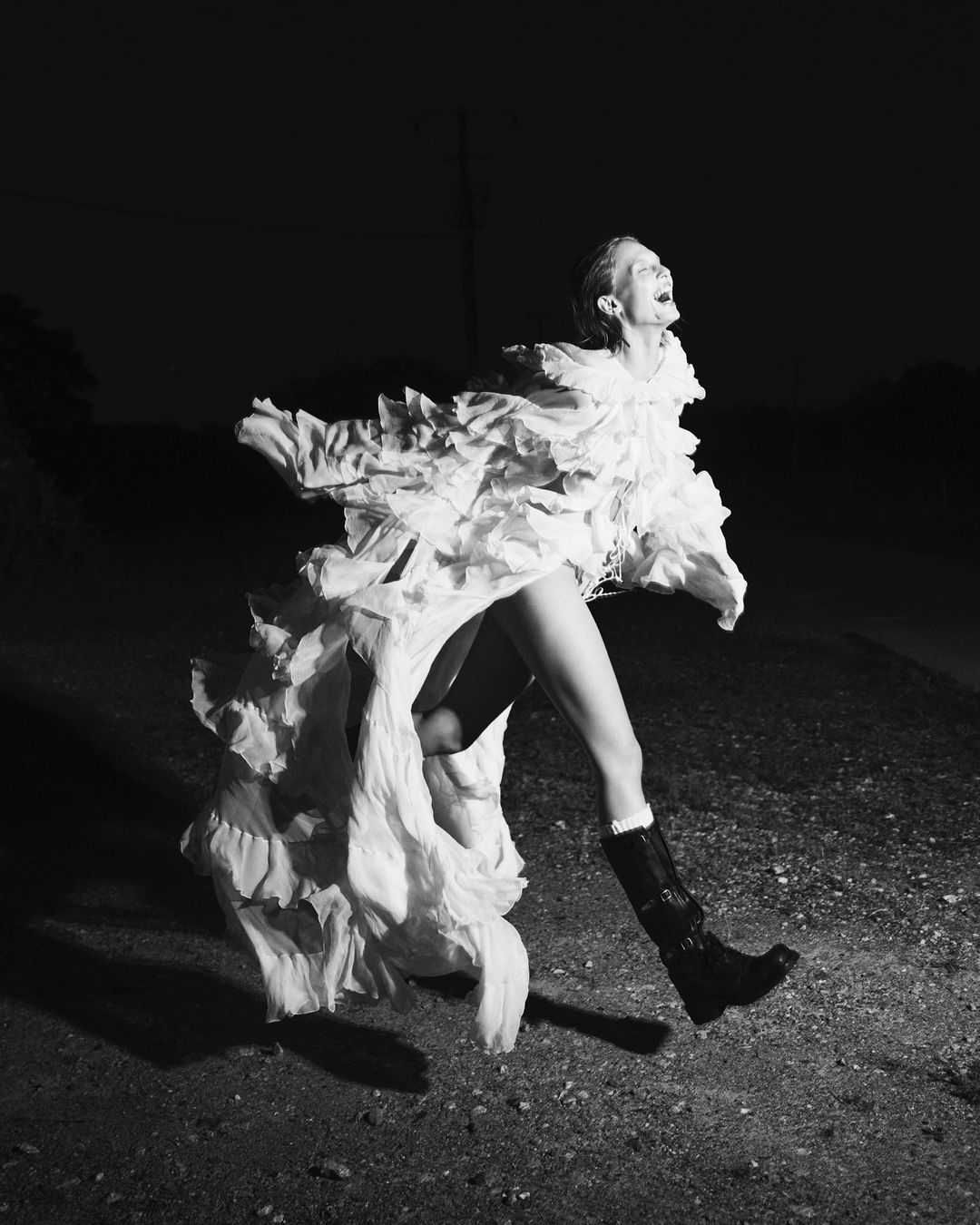 A woman in a ruffled dress strikes a pose, her mouth open in an expressive display of emotion in a black and white fashion portrait.