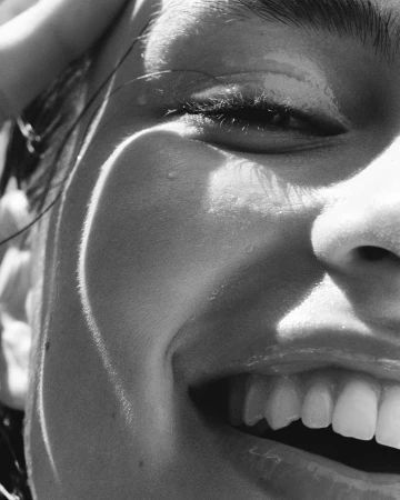 Close-up black and white portrait of a smiling person with wet skin and glistening lips, photographed in Paris.