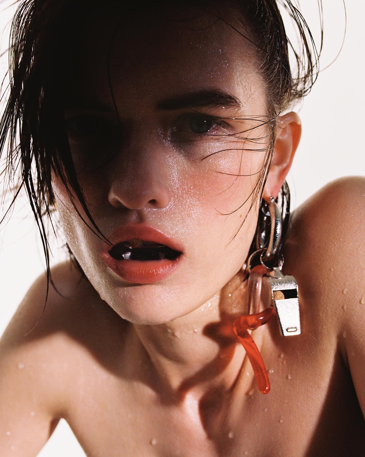 Close-up portrait of a fair-skinned adult woman with wet hair, red lips, silver earrings and a silver whistle against a white background.