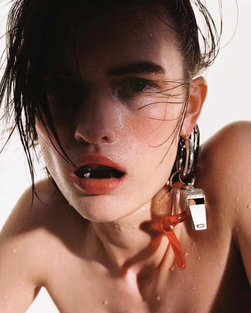 Close-up portrait of a fair-skinned adult woman with wet hair, red lips, silver earrings and a silver whistle against a white background.