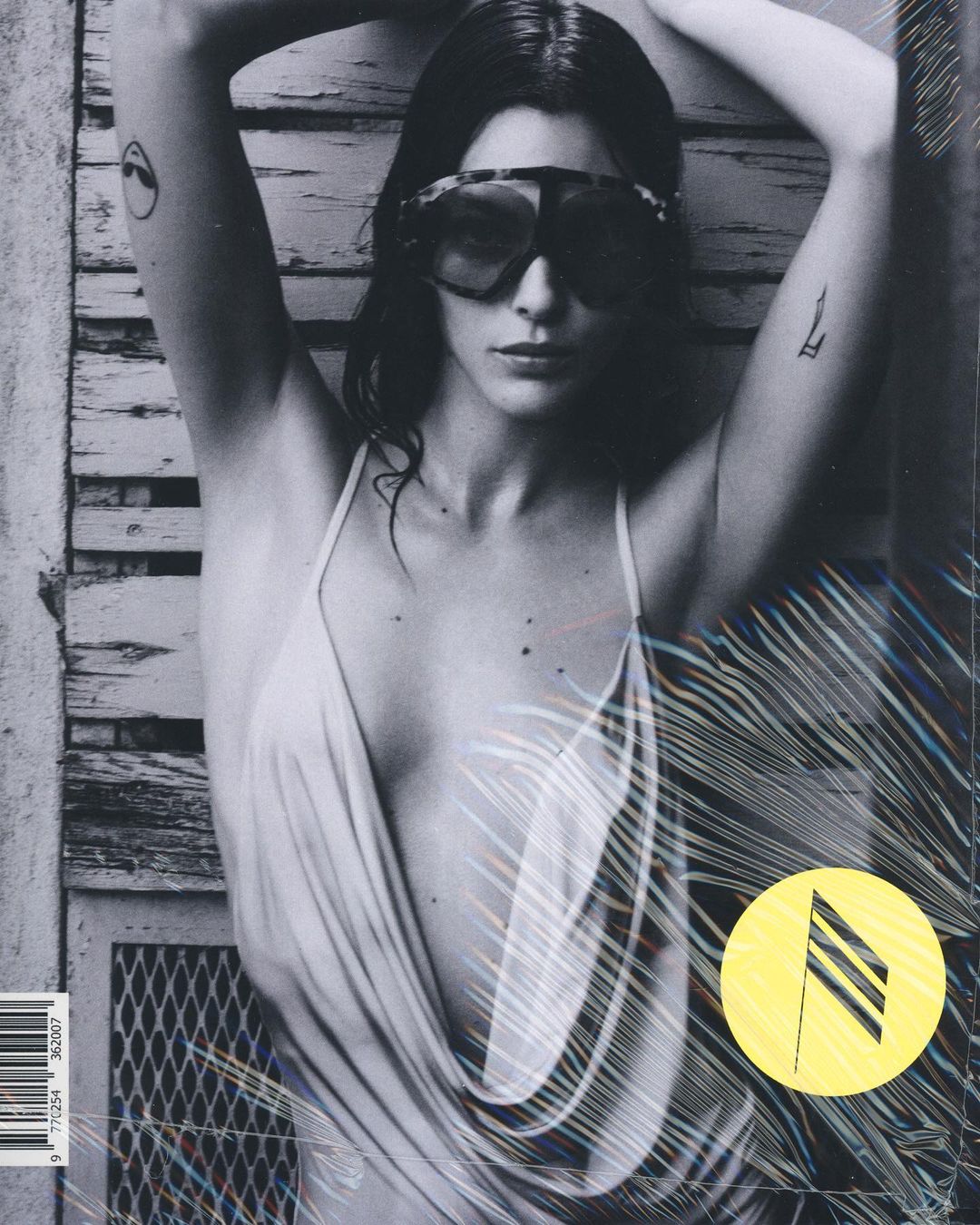 Black and white magazine cover featuring a young woman wearing sunglasses and a low-cut dress, with a textured background.