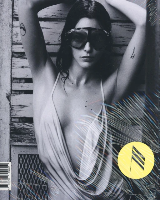 Black and white magazine cover featuring a young woman wearing sunglasses and a low-cut dress, with a textured background.