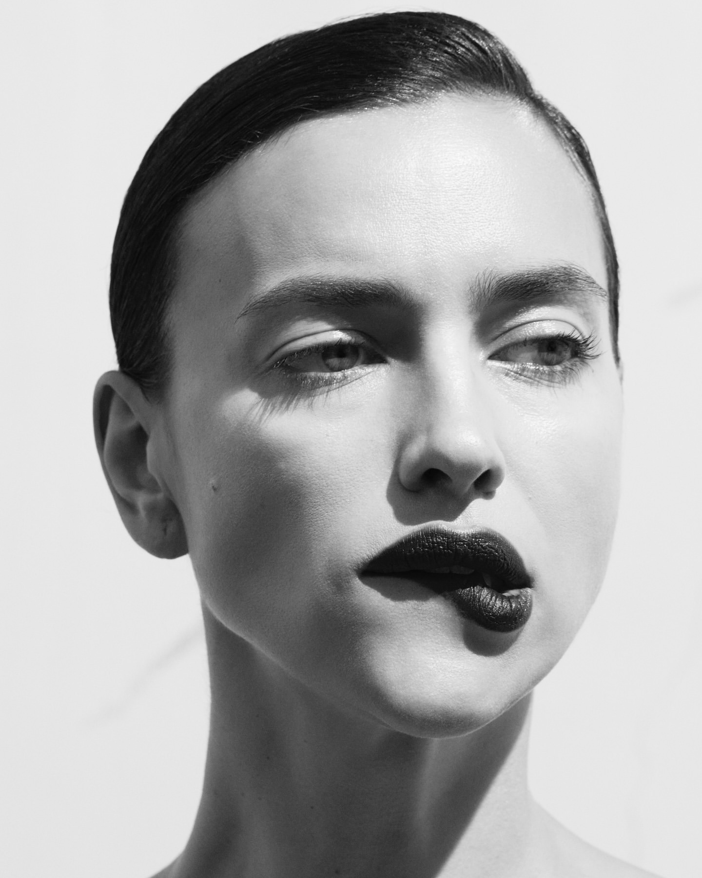 Monochrome portrait of an adult woman with dark lipstick, styled hair, and light skin in a bright, minimalist setting. Beauty shot.