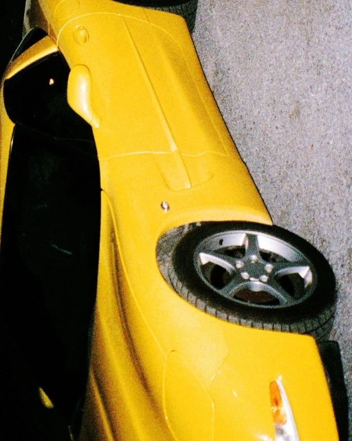 A striking close-up showcases a vibrant yellow sports car, highlighting its sleek design and powerful presence against a muted grey background.