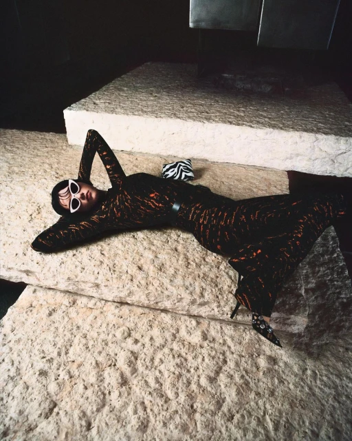 Fashion shot of a woman in a patterned dress lying on a stone surface wearing sunglasses with a zebra-print purse nearby.