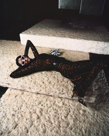 Fashion shot of a woman in a patterned dress lying on a stone surface wearing sunglasses with a zebra-print purse nearby.