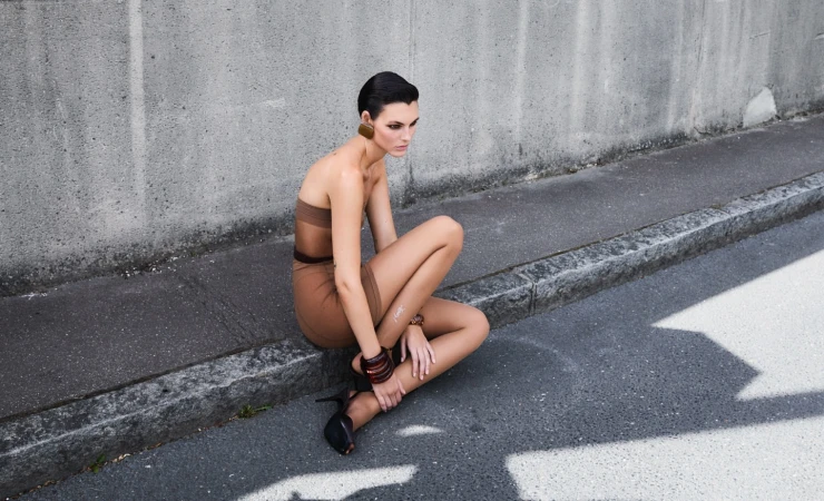 Model in brown strapless dress squatting by a concrete curb in Paris, photographed by Vito Fernicola.