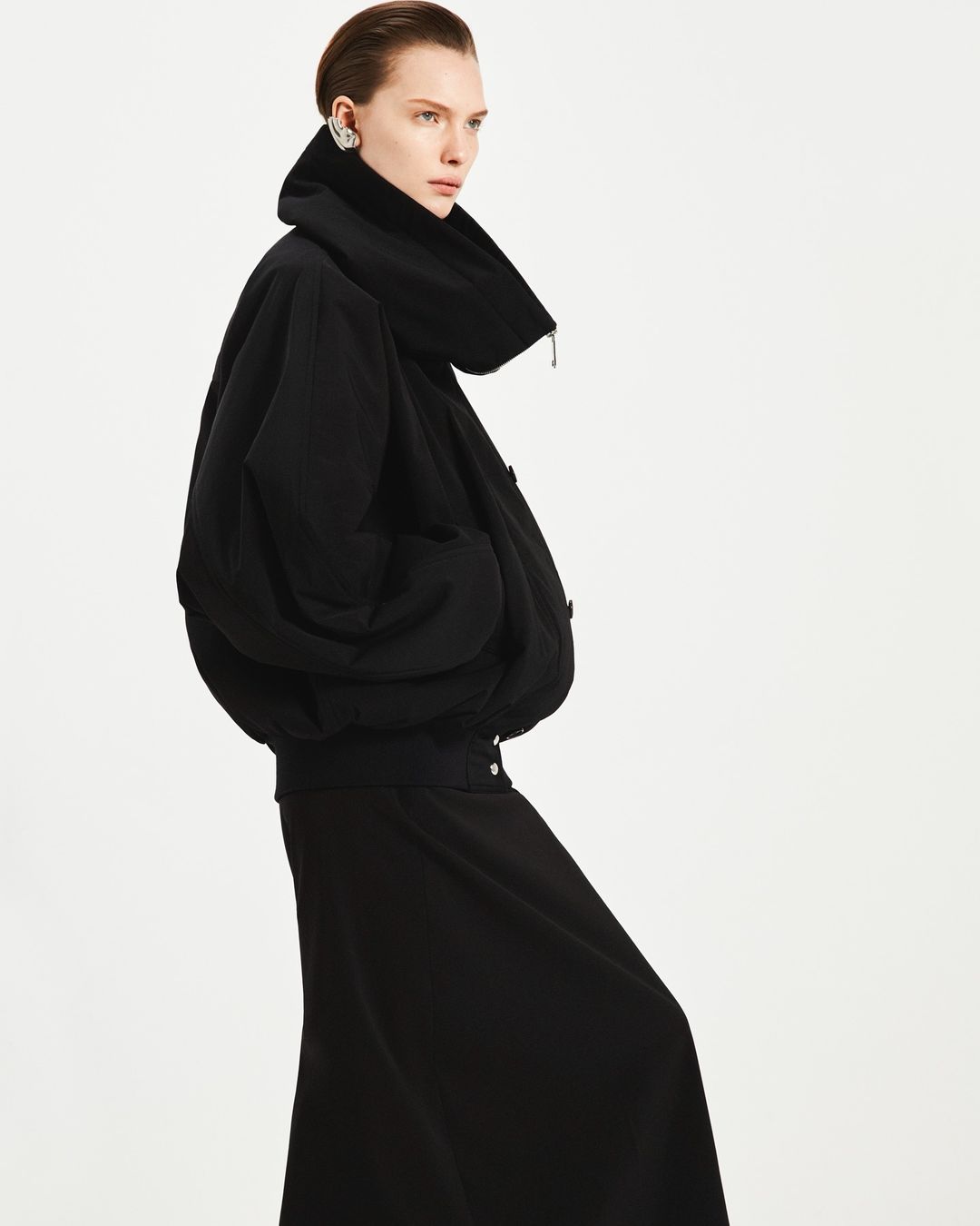 Model in a black oversized jacket and skirt against a bright white background by photographer Vito Fernicola.