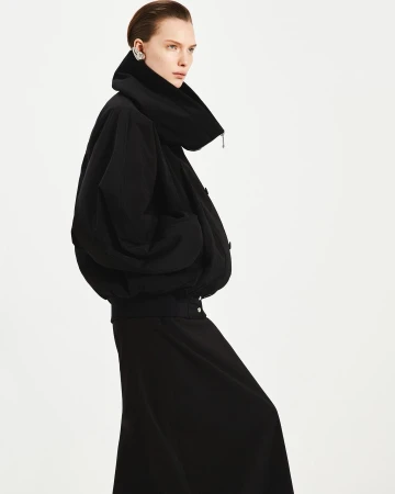 Model in a black oversized jacket and skirt against a bright white background by photographer Vito Fernicola.