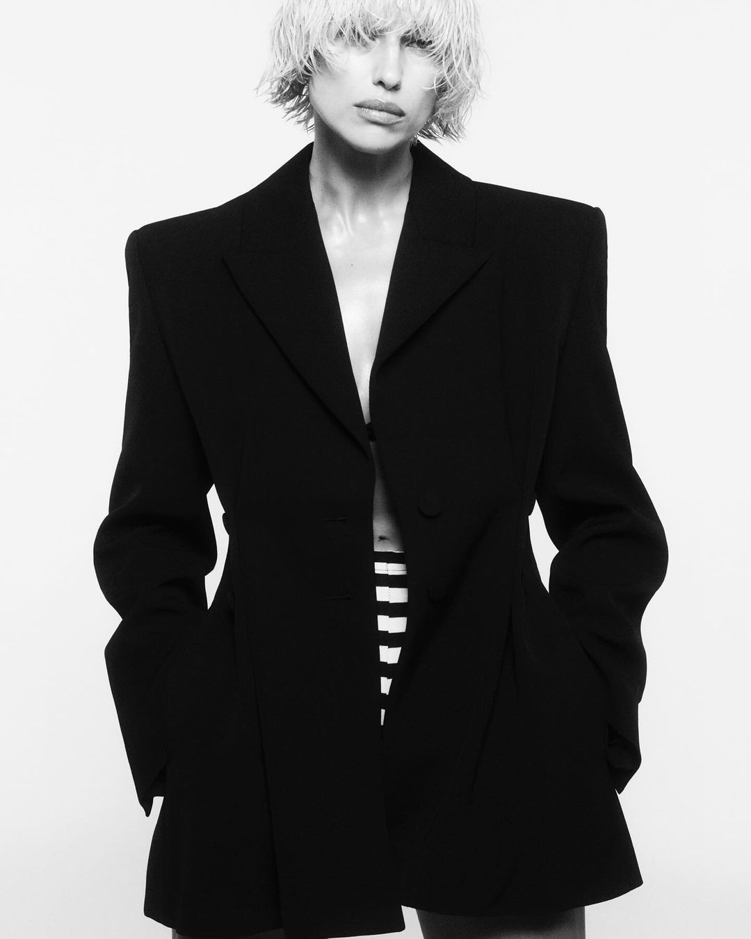 Monochrome portrait of a woman wearing a black blazer and striped bottoms in a studio setting with soft lighting.