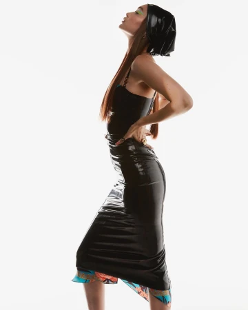 Model in shiny black latex dress and matching headscarf posing against a bright white background