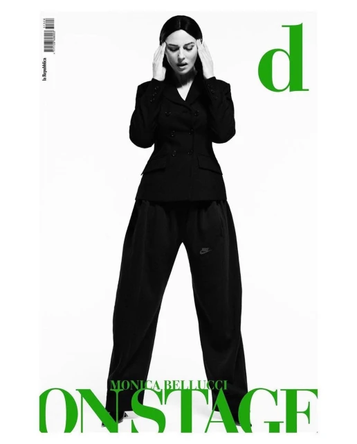 Monica Bellucci poses in a black double-breasted blazer and baggy pants against a white backdrop, hands to her head. Magazine cover.