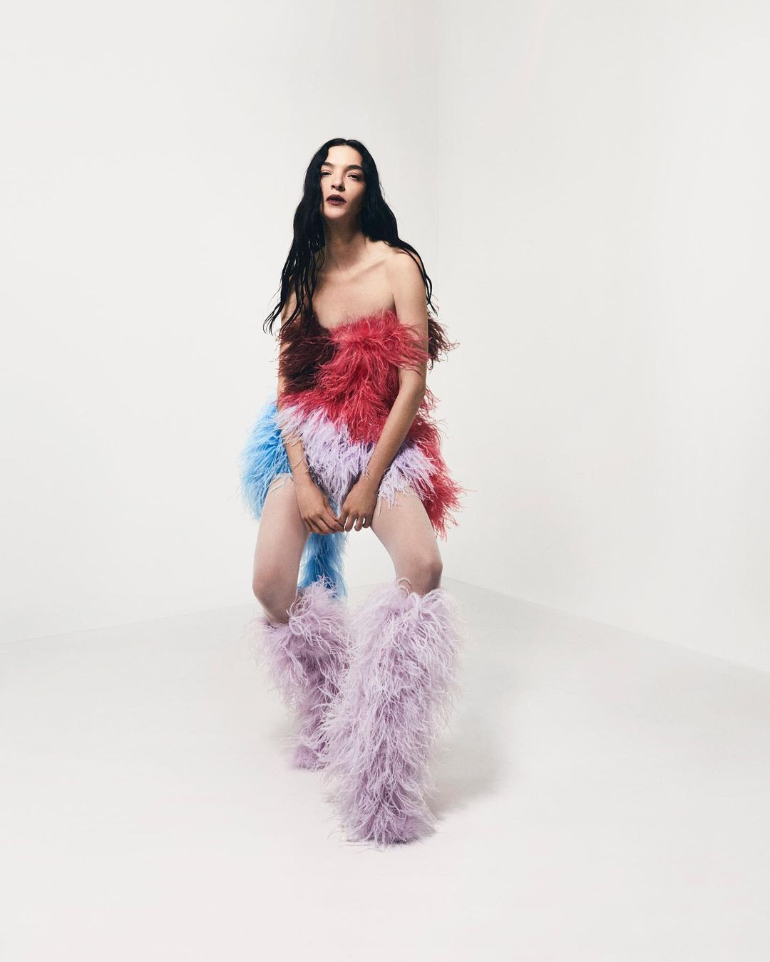 Fashion model in a feathered dress and feathered boots poses in a bright photo studio, showcasing a unique and avant-garde style.
