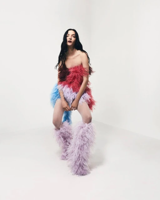 Fashion model in a feathered dress and feathered boots poses in a bright photo studio, showcasing a unique and avant-garde style.