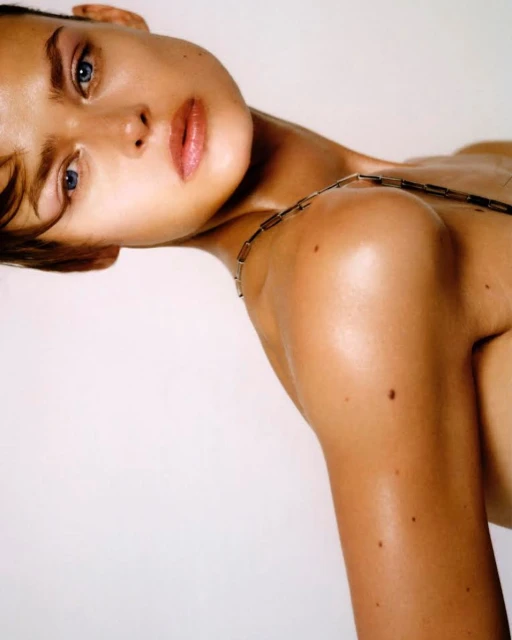 A close-up studio portrait of an adult female model with light skin and short hair, wearing a necklace, against a white background.