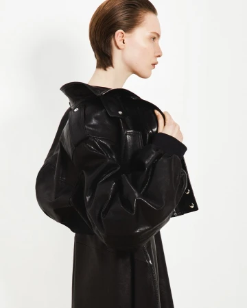 Fashion shot of a woman in a black leather jacket and dress against a bright white background in a studio setting, side view.