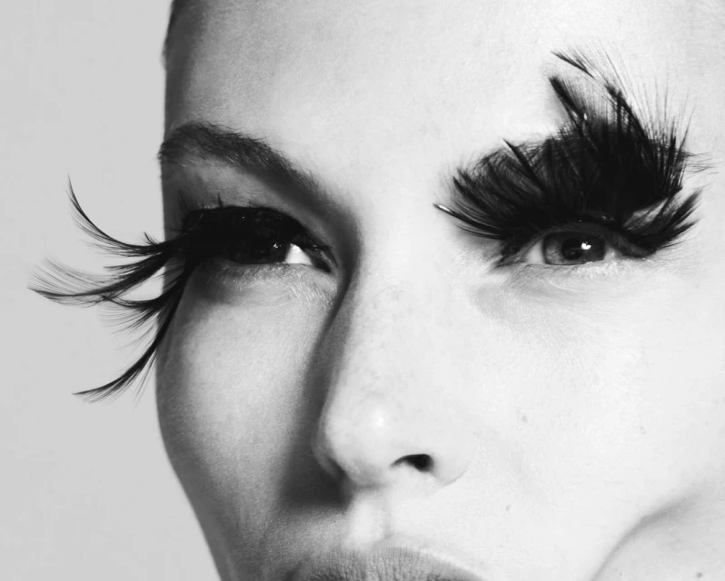 Close-up black and white portrait of a woman with dramatic black feathered eyelashes, emphasizing beauty and makeup.