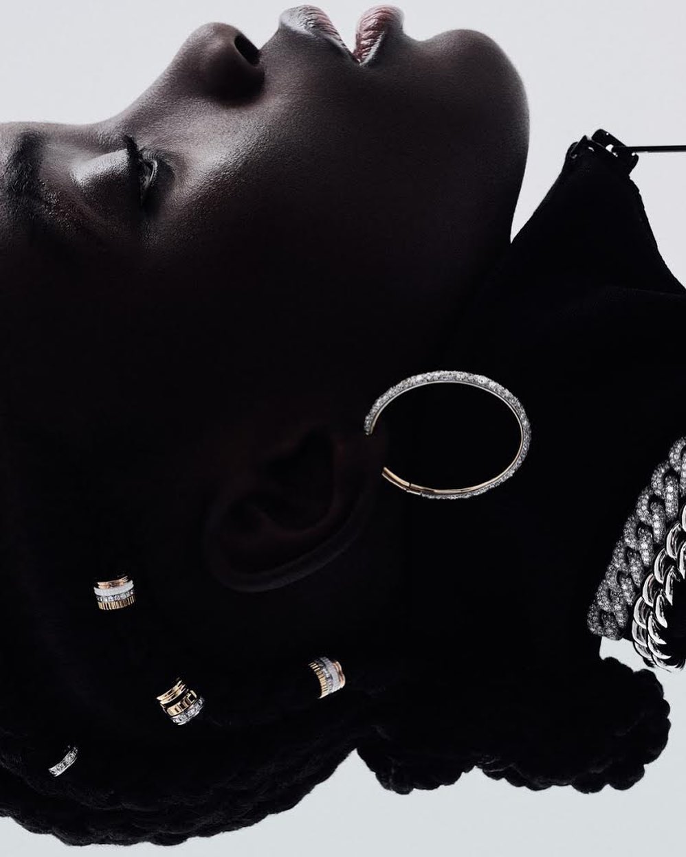 Close-up of a dark-skinned woman wearing silver and diamond earrings and a necklace while lying on her back in a studio.