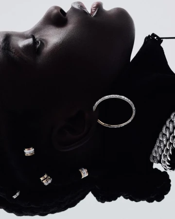 Close-up of a dark-skinned woman wearing silver and diamond earrings and a necklace while lying on her back in a studio.