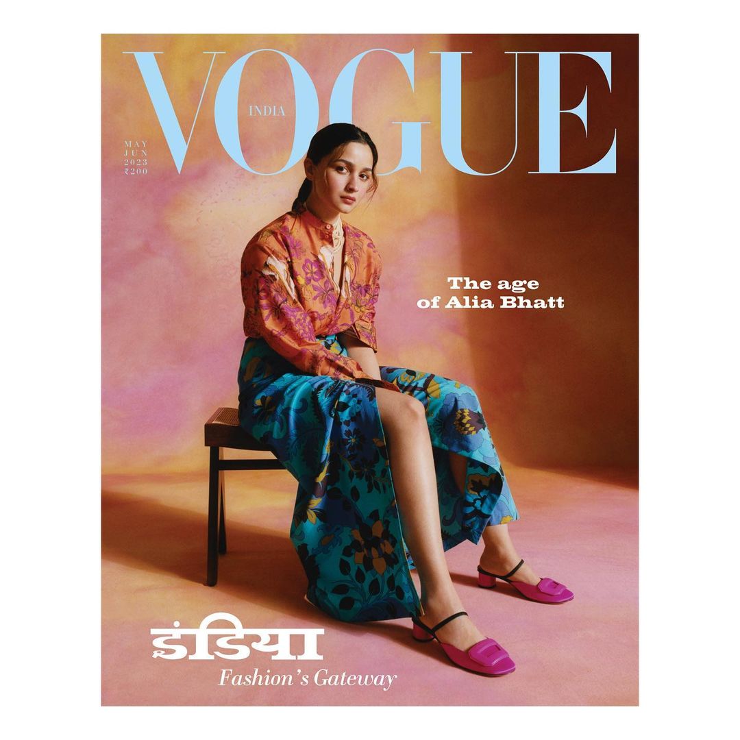 Vogue India magazine cover featuring Alia Bhatt wearing patterned shirt and skirt, seated on a wooden chair against a textured backdrop.