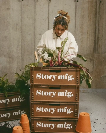 Adult female tending a crate garden with beet greens on a cement backdrop, wearing a white jacket, with terracotta pots nearby.