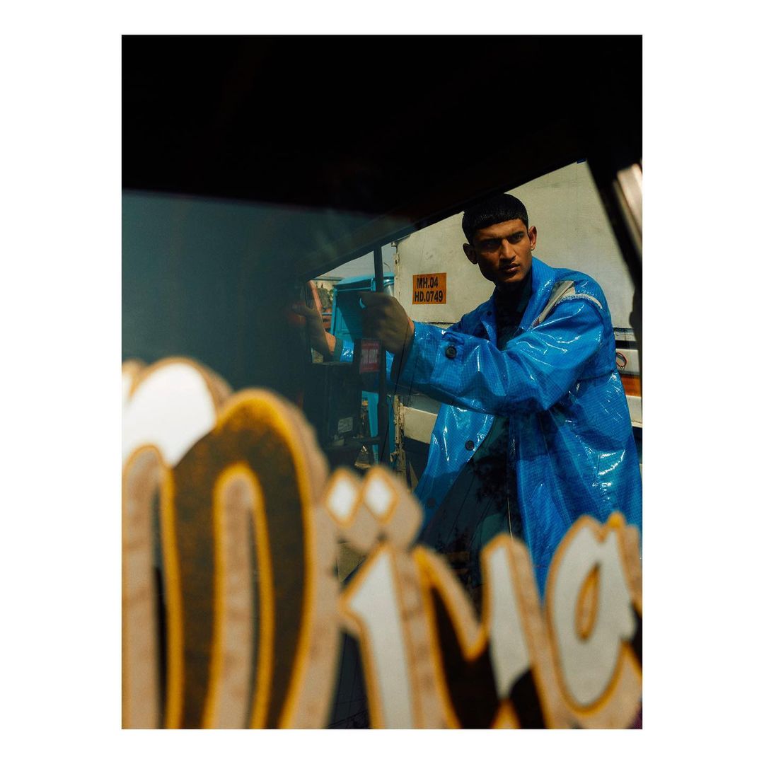 Fashionable adult male in a blue plastic raincoat poses outside with graffiti in the foreground, creating a stylish and urban image.