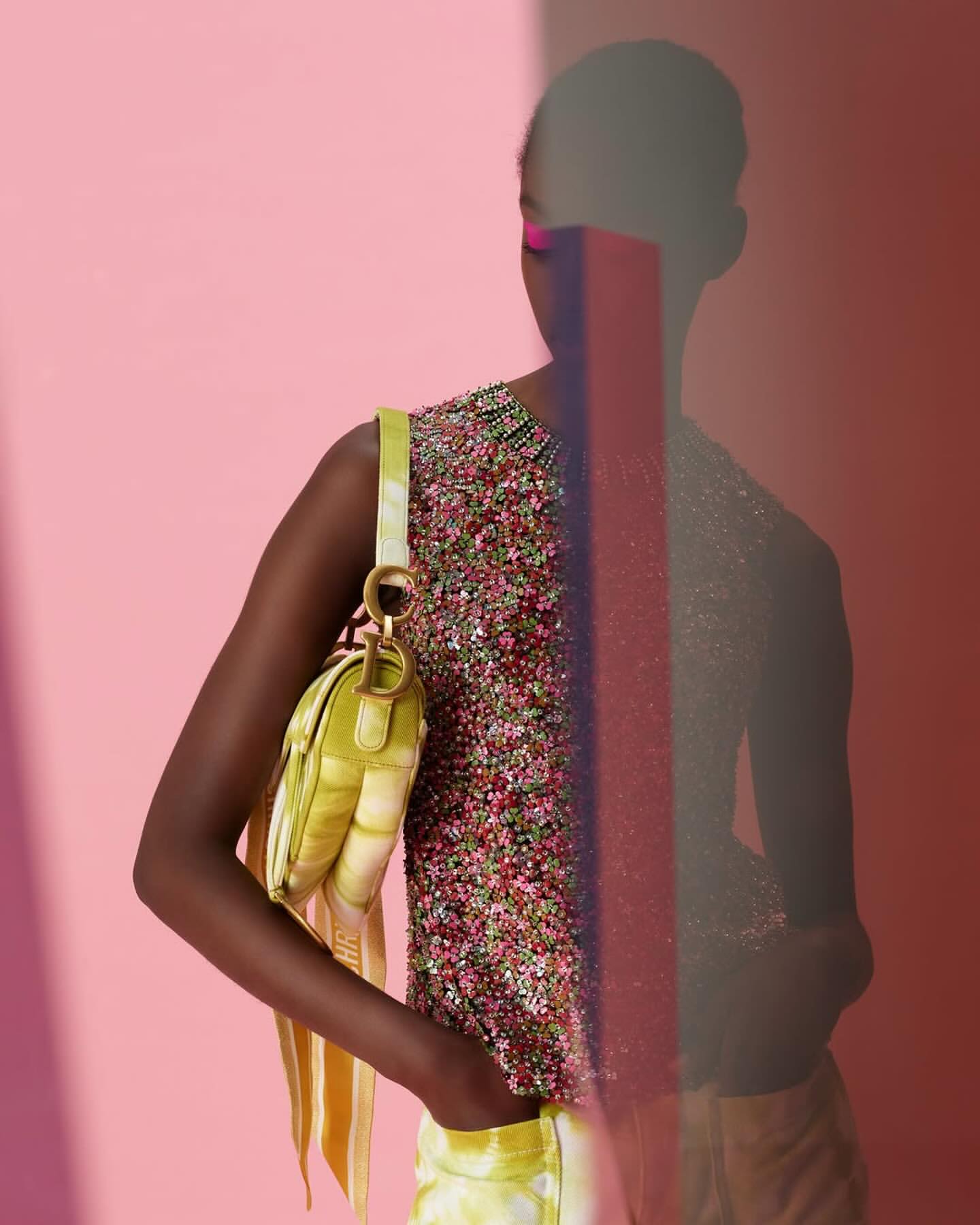 Fashionable woman poses indoors against a pink background with lime green purse and beaded top; an abstract transparent block.