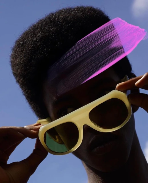 Close-up of a Black person wearing cream-colored sunglasses and looking up at the sky with an overlaid pink brushstroke effect.