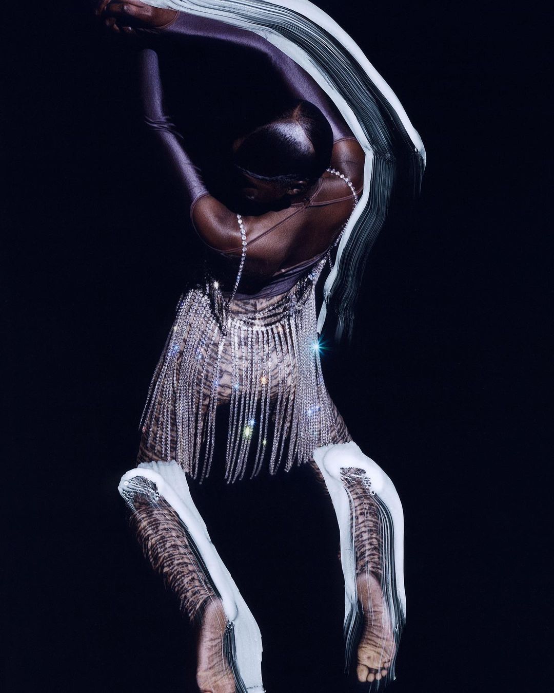 Woman in rhinestones poses in studio. Elegant fashion photograph shows adult female in shiny dress and leggings on dark background.