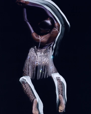 Woman in rhinestones poses in studio. Elegant fashion photograph shows adult female in shiny dress and leggings on dark background.