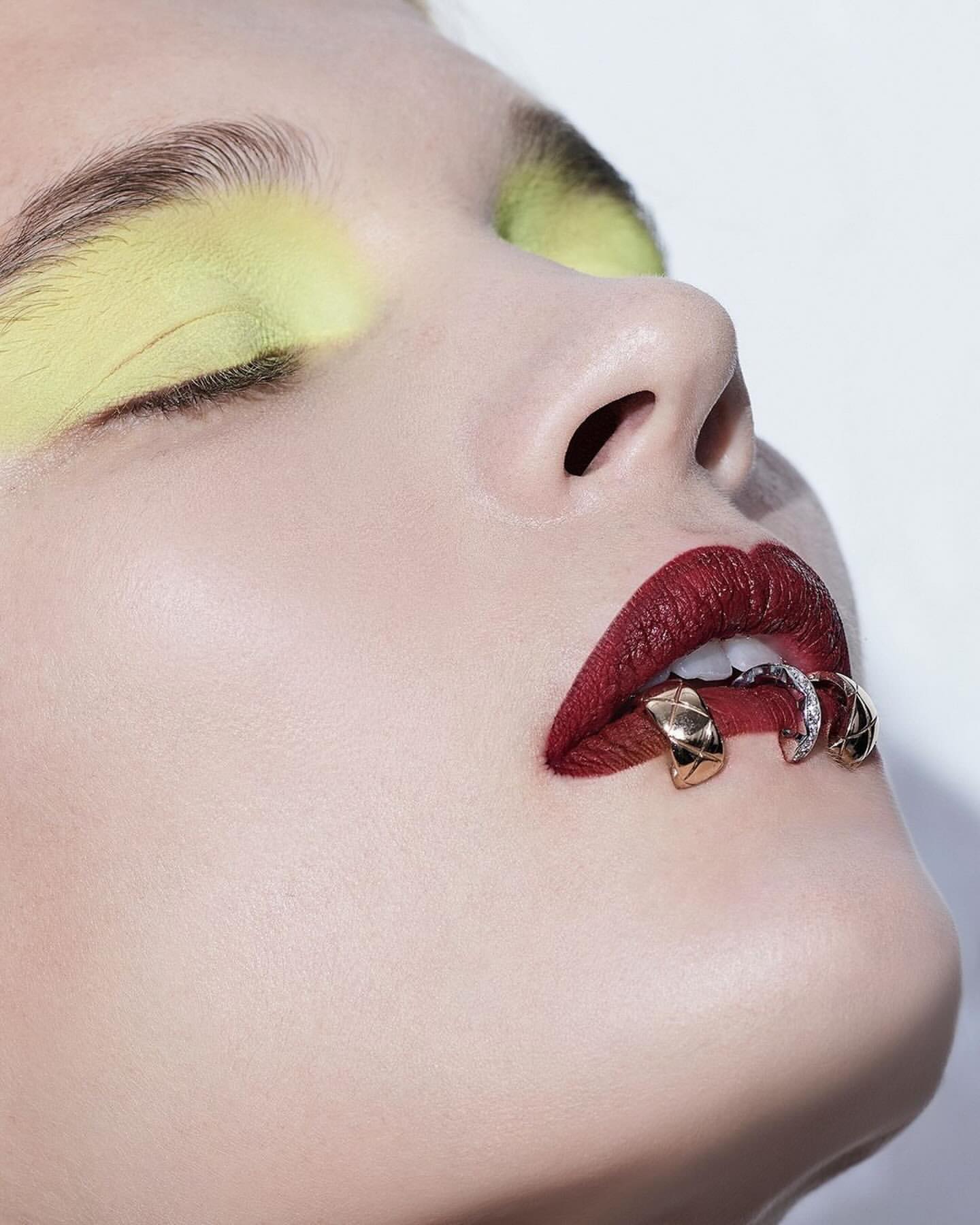 Close-up beauty shot of a woman with creative makeup and lip jewelry against a white backdrop, emphasizing the beauty and fashion elements.