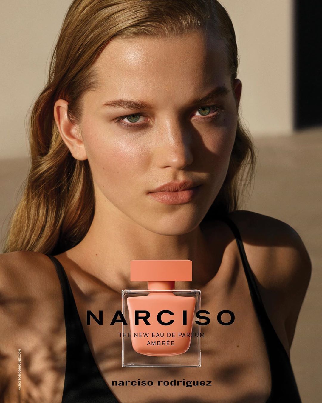Close-up studio shot of a fair-skinned woman with a Narciso Rodriguez perfume bottle, featuring warm lighting and a minimalistic backdrop.