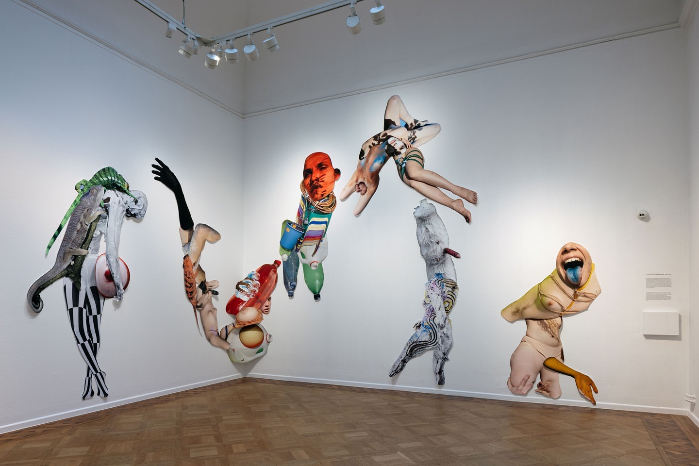 Art installation featuring human figures and torsos combined with objects displayed in an art gallery setting, creating a surreal collage.