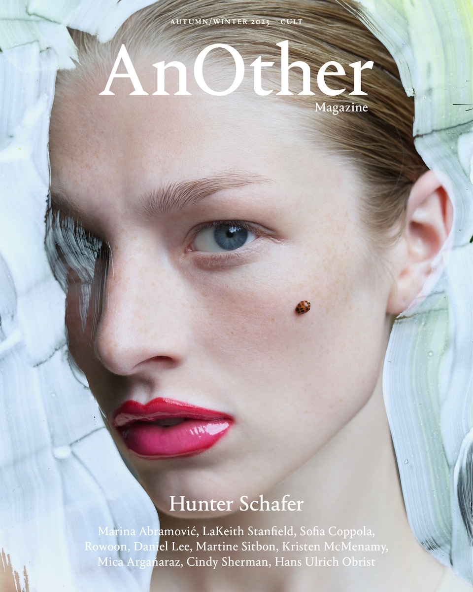 Magazine cover featuring a portrait of a young woman with fair skin, blue eyes, and red lipstick, with artistic white brushstrokes.