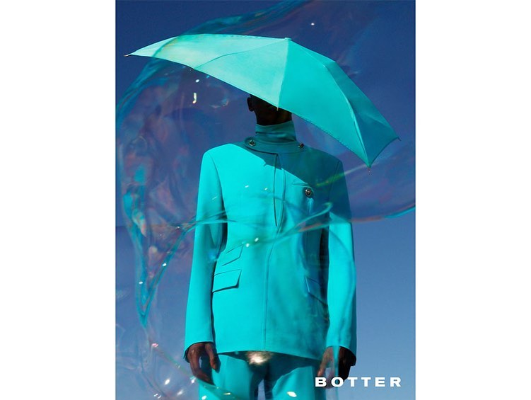 Fashionable person in blue suit holding blue umbrella, artistic light and dark background, BOTTER logo in bottom-right corner.