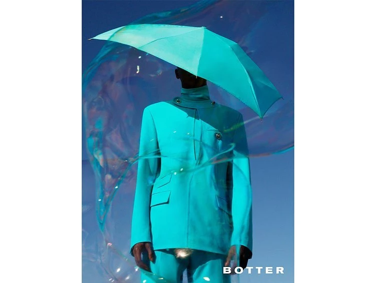 Fashionable person in blue suit holding blue umbrella, artistic light and dark background, BOTTER logo in bottom-right corner.