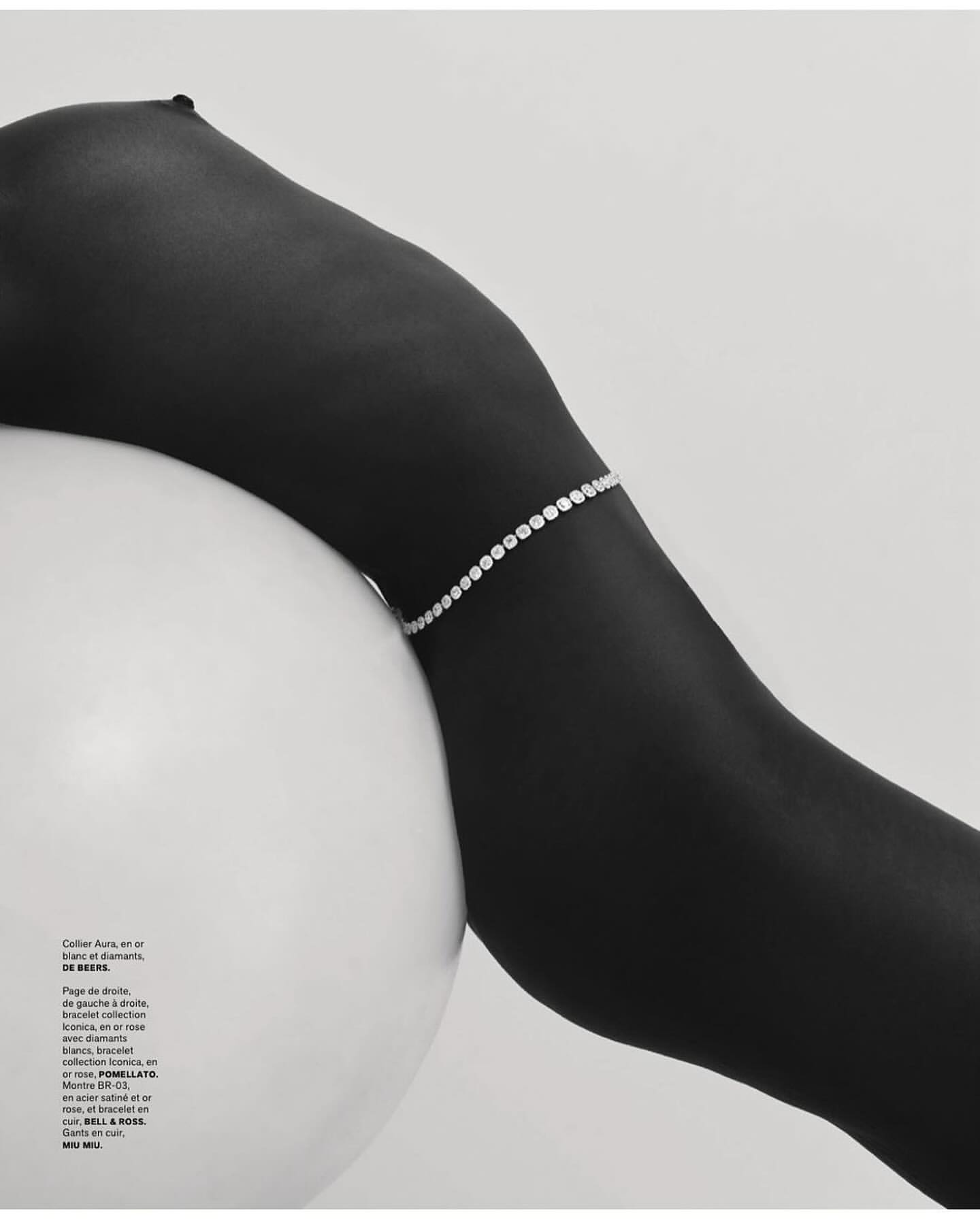 Woman's dark skin is adorned with a diamond bracelet, contrasting against a white spherical prop and clean background.