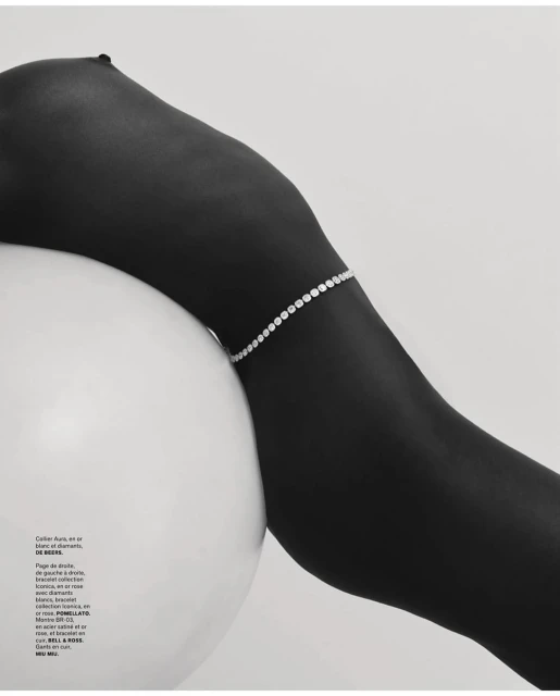 Woman's dark skin is adorned with a diamond bracelet, contrasting against a white spherical prop and clean background.